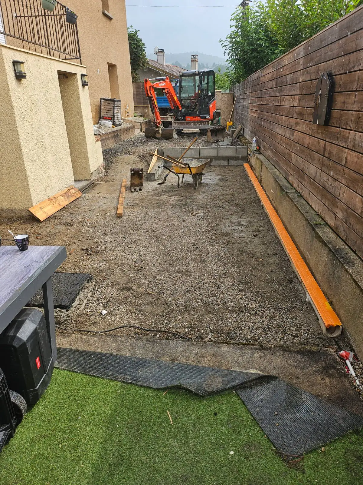 Terrassement d'une allée étroite entre une maison et une palissade, mini-pelle et brouette au fond