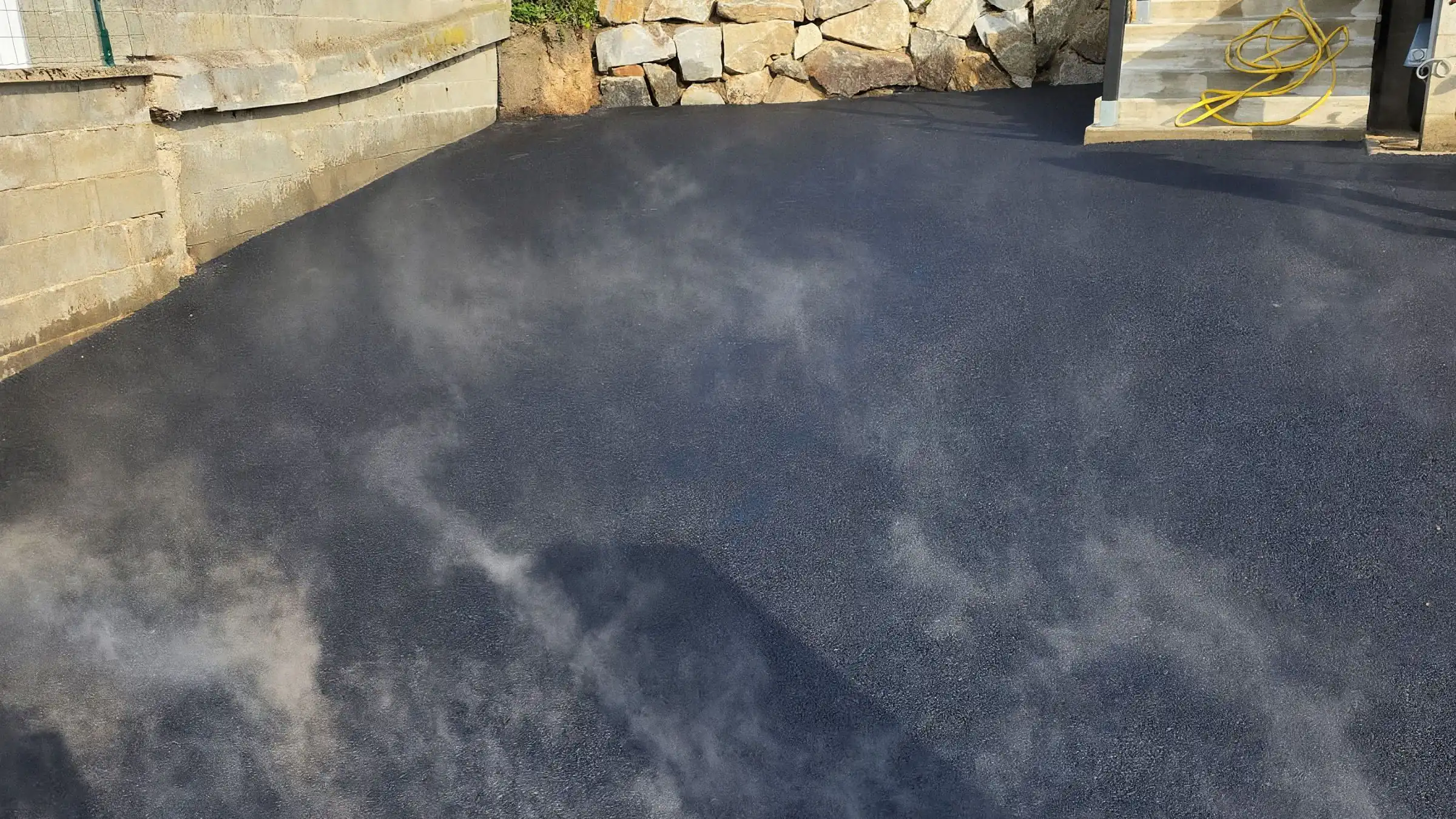 Enrobé encore chaud dégageant de la vapeur dans une cour fraîchement revêtue, caniveau à grille au premier plan