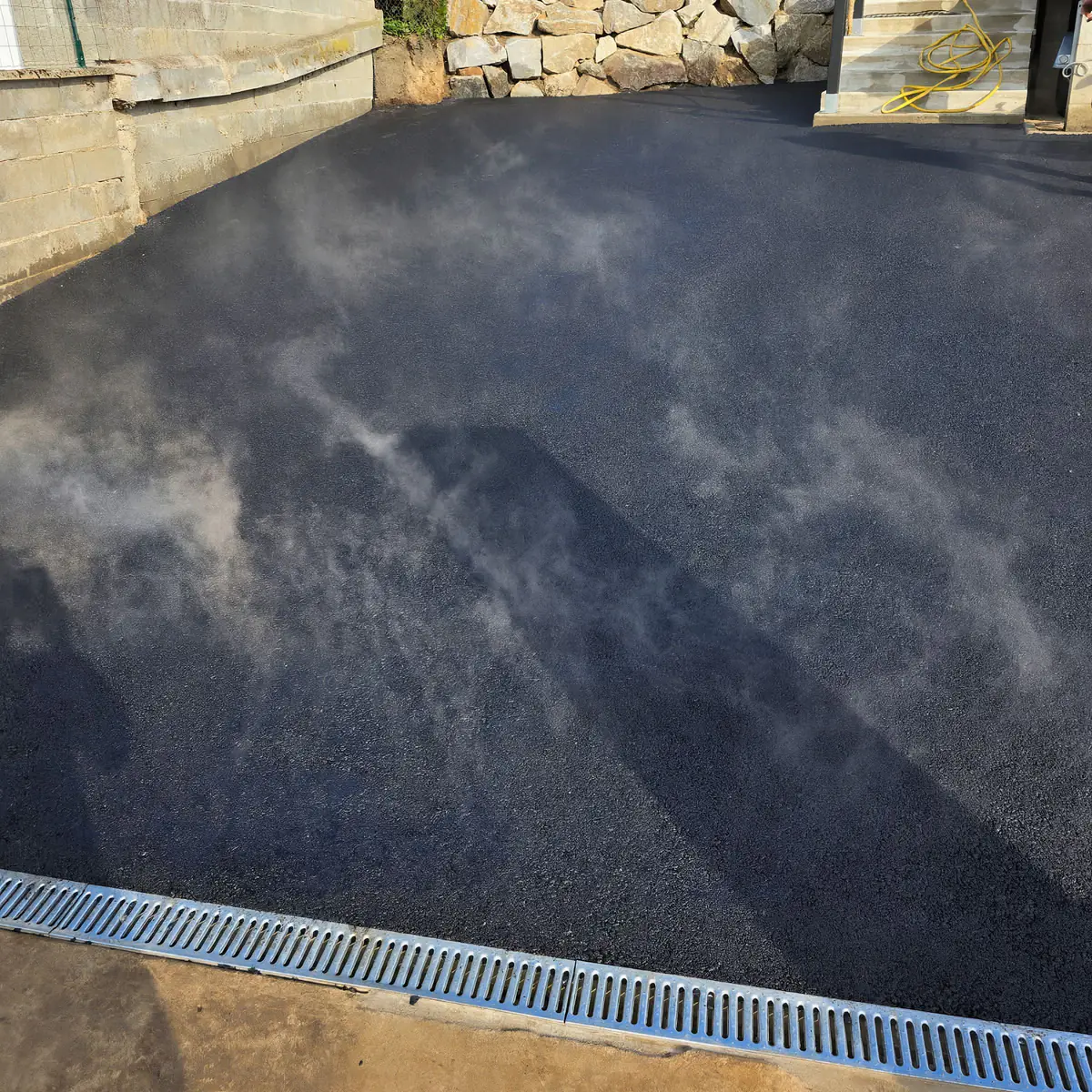 Enrobé encore chaud dégageant de la vapeur dans une cour fraîchement revêtue, caniveau à grille au premier plan