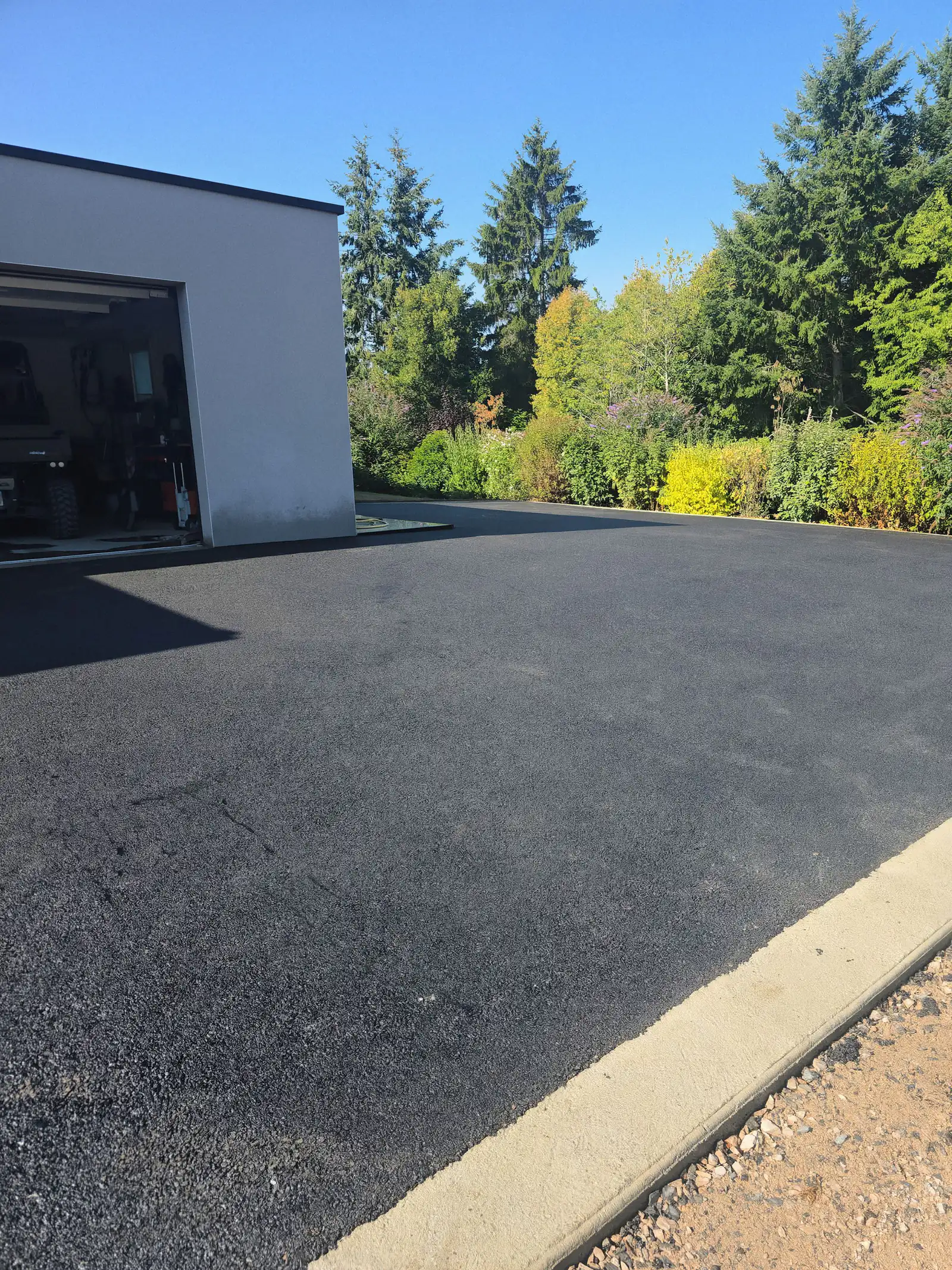 Après travaux : cour en enrobé neuf devant un garage contemporain, bordée d'une bordure béton